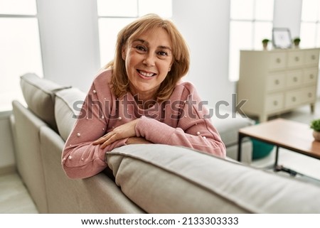 Middle age blonde woman smiling happy relaxed sitting on the sofa at home.