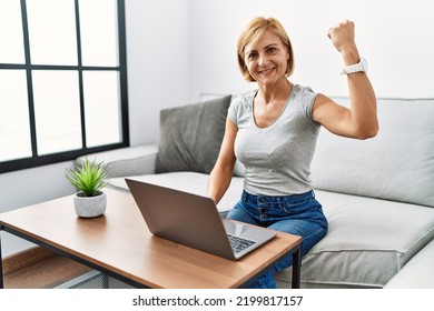 Middle Age Blonde Woman Using Laptop At Home Strong Person Showing Arm Muscle, Confident And Proud Of Power 