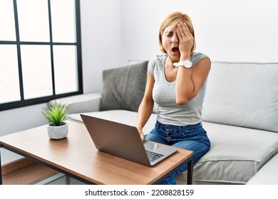 Middle Age Blonde Woman Using Laptop At Home Yawning Tired Covering Half Face, Eye And Mouth With Hand. Face Hurts In Pain. 