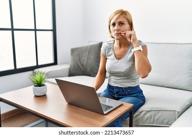 Middle Age Blonde Woman Using Laptop At Home Mouth And Lips Shut As Zip With Fingers. Secret And Silent, Taboo Talking 