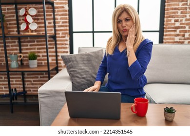 Middle Age Blonde Woman Using Computer Laptop At Home Touching Mouth With Hand With Painful Expression Because Of Toothache Or Dental Illness On Teeth. Dentist 