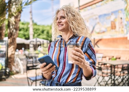 Middle age blonde woman using smartphone drinking coffee at terrace coffee shop