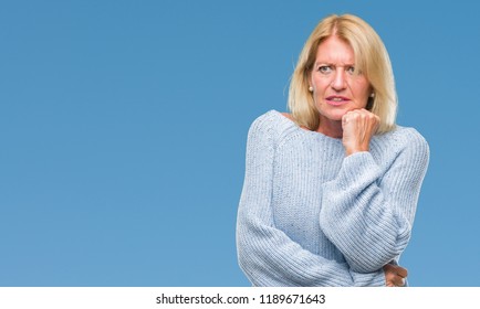 Blonde Frau im Mittelalter, die Winterpullover auf isoliertem Hintergrund trägt und gestresst und nervös aussieht, mit Händen auf Mund beißenden Nägeln. Angstprobleme.