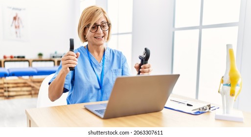Middle age blonde woman wearing physio therapy uniform doing tele rehab using hand grip at clinic - Shutterstock ID 2063307611