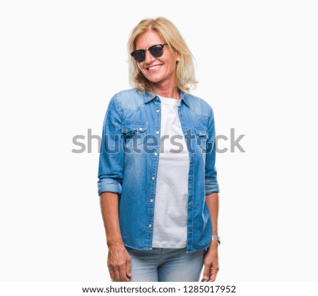 Middle age blonde woman wearing sunglasses over isolated background looking away to side with smile on face, natural expression. Laughing confident.