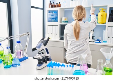 Middle Age Blonde Woman Working At Scientist Laboratory Posing Backwards Pointing Ahead With Finger Hand 