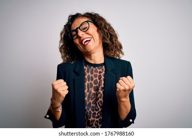Middle age brunette business woman wearing glasses standing over isolated white background very happy and excited doing winner gesture with arms raised, smiling and screaming for success. Celebration.