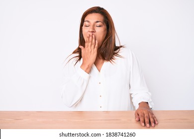 Middle Age Brunette Hispanic Business Woman Wearing Casual White Shirt Sitting On The Table Bored Yawning Tired Covering Mouth With Hand. Restless And Sleepiness. 