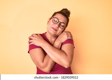 Middle age brunette hispanic woman wearing casual clothes and glasses hugging oneself happy and positive, smiling confident. self love and self care 