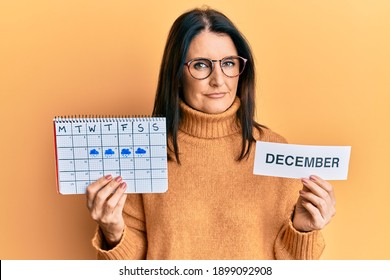 Middle Age Brunette Woman Holding December Calendar Relaxed With Serious Expression On Face. Simple And Natural Looking At The Camera. 