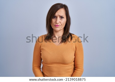 Middle age brunette woman standing wearing orange sweater depressed and worry for distress, crying angry and afraid. sad expression. 