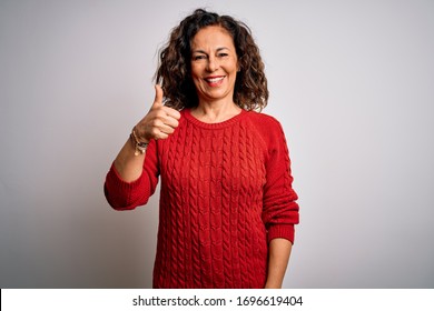 Middle age brunette woman wearing casual sweater standing over isolated white background doing happy thumbs up gesture with hand. Approving expression looking at the camera showing success.