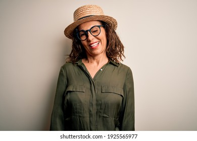 Middle Age Brunette Woman Wearing Glasses And Hat Standing Over Isolated White Background Winking Looking At The Camera With Sexy Expression, Cheerful And Happy Face.