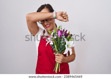 Middle age brunette woman wearing apron working at florist shop holding bouquet smiling cheerful playing peek a boo with hands showing face. surprised and exited 