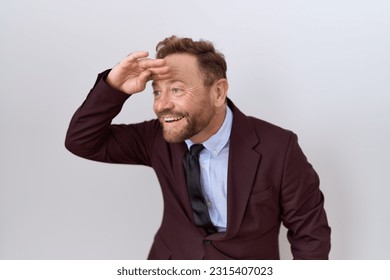 Middle age business man with beard wearing suit and tie very happy and smiling looking far away with hand over head. searching concept.  - Shutterstock ID 2315407023