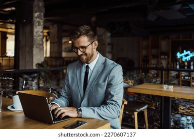 Middle age businessman sitting in cafe bar and enjoying at coffee break between two meetings. He uses laptop computer and he is positive and confident.  - Powered by Shutterstock