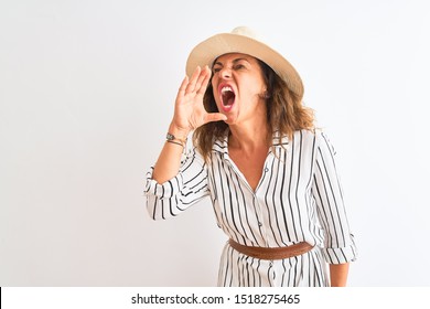 Middle age businesswoman wearing striped dress and hat over isolated white background shouting and screaming loud to side with hand on mouth. Communication concept.