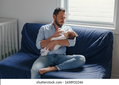 Middle age Caucasian father feeding newborn baby from bottle milk. Man parent holding rocking child on his hands. Authentic lifestyle candid real moment. Single dad family home life concept. - Powered by Shutterstock