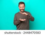 Middle age caucasian man isolated on blue background holding copyspace imaginary on the palm to insert an ad