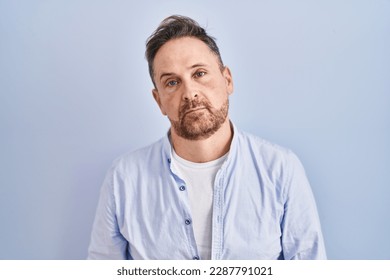 Middle age caucasian man standing over blue background looking sleepy and tired, exhausted for fatigue and hangover, lazy eyes in the morning.  - Powered by Shutterstock