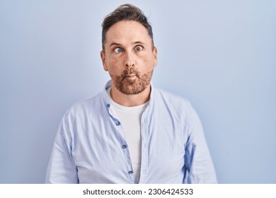 Middle age caucasian man standing over blue background making fish face with lips, crazy and comical gesture. funny expression. 