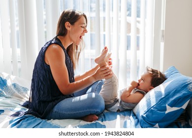 Middle Age Caucasian Mother Playing With Boy Toddler Son. Mom And Child Baby Having Fun On Bed In Bedroom At Home. Happy Authentic Family Childhood Lifestyle. Tender Touching Sweet Moments