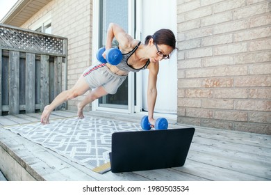 Middle Age Caucasian Woman Doing Push-ups Exercises With Dumb-bells On Home Backyard Online. Video Fitness Sport Workout On Internet. Woman Learning In Training Class With Laptop. Sport At Home