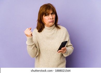 Middle Age Caucasian Woman Holding A Phone Showing Fist To Camera, Aggressive Facial Expression.