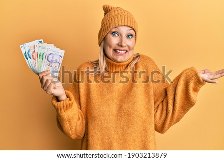 Middle age caucasian woman holding singapore dollars banknotes celebrating achievement with happy smile and winner expression with raised hand 