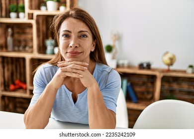 Middle age caucasian woman smiling happy sitting on the table at home. - Shutterstock ID 2235242109