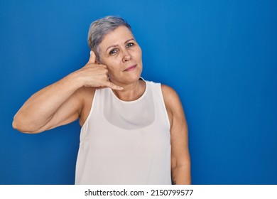 Middle Age Caucasian Woman Standing Over Blue Background Smiling Doing Phone Gesture With Hand And Fingers Like Talking On The Telephone. Communicating Concepts. 