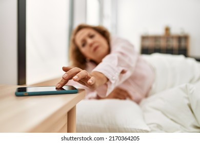 Middle age caucasian woman turning off smartphone alarm clock lying on the bed at bedroom. - Powered by Shutterstock