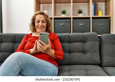 Middle Age Caucasian Woman Using Smartphone Sitting On The Sofa At Home.