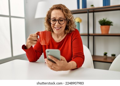 Middle age caucasian woman using smartphone and drinking coffee sitting on the sofa at home. - Powered by Shutterstock