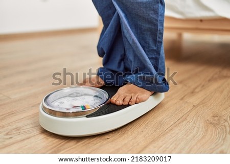 Middle age caucasian woman using weighing machine at home