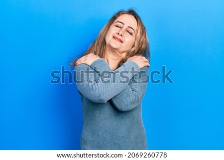 Middle age caucasian woman wearing casual clothes hugging oneself happy and positive, smiling confident. self love and self care 