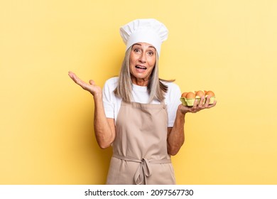 Middle Age Chef Woman Feeling Happy, Excited, Surprised Or Shocked, Smiling And Astonished At Something Unbelievable Holding An Eggs Box