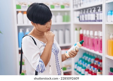 Middle age chinese woman customer holding shampoo bottle at pharmacy - Powered by Shutterstock