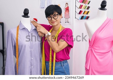 Middle age chinese woman tailor smiling confident leaning on manikin at atelier