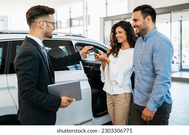 Middle age couple buys a car at a car dealership. The seller gives them the car keys. They are very happy. - Powered by Shutterstock