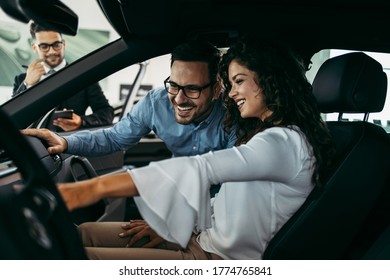 Middle age couple choosing and buying car at car showroom. Car salesman helps them to make right decision. - Shutterstock ID 1774765841