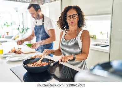 Middle Age Couple Cooking Mediterranean Food At Home Thinking Attitude And Sober Expression Looking Self Confident 