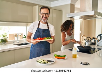 Middle Age Couple Cooking Mediterranean Food At Home Smiling With A Happy And Cool Smile On Face. Showing Teeth. 