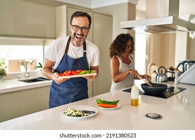 Middle Age Couple Cooking Mediterranean Food At Home Smiling And Laughing Hard Out Loud Because Funny Crazy Joke. 