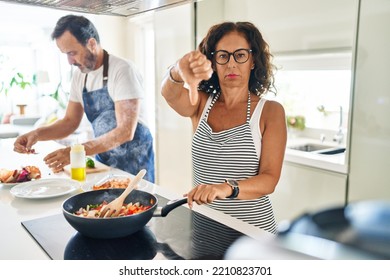 Middle Age Couple Cooking Mediterranean Food At Home With Angry Face, Negative Sign Showing Dislike With Thumbs Down, Rejection Concept 