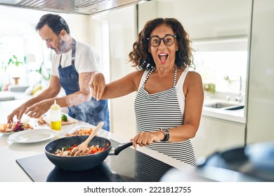 Middle Age Couple Cooking Mediterranean Food At Home Smiling Happy Pointing With Hand And Finger 