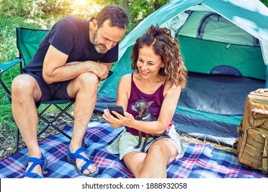 Middle Age Couple  Of Hiker Smiling Happy Camping At The Forest. Sitting On The Floor Using Smartphone.