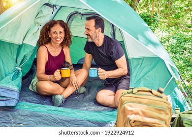 Middle Age Couple  Of Hiker Smiling Happy Looking At The Camera. Drinking Coffee Camping At The Forest.