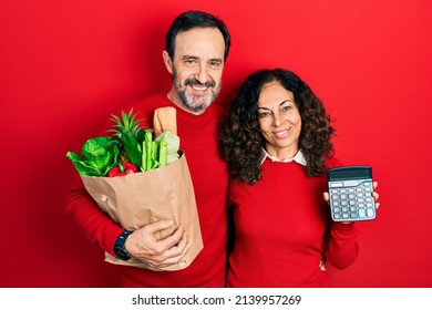 Middle Age Couple Of Hispanic Woman And Man Holding Groceries Bag And Calculator Smiling With A Happy And Cool Smile On Face. Showing Teeth. 