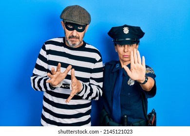 Middle age couple of hispanic woman and man wearing thief and police uniform doing stop sing with palm of the hand. warning expression with negative and serious gesture on the face. 
